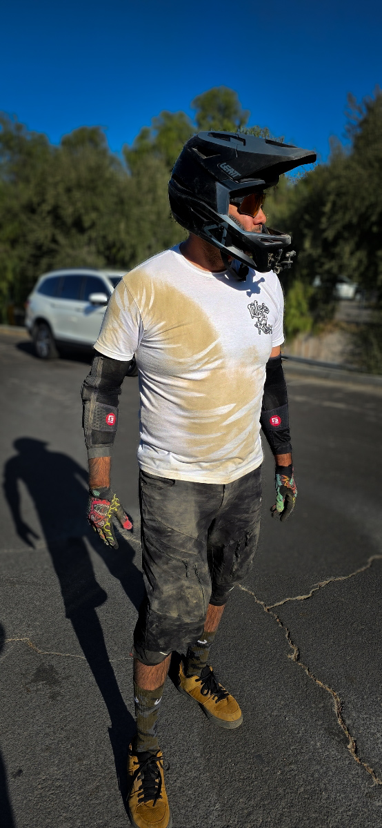 A helmeted mountain biker wearing a white Cranked shirt covered in trail dirt